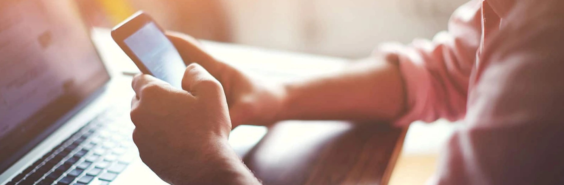 Close-up of hands with a phone and laptop